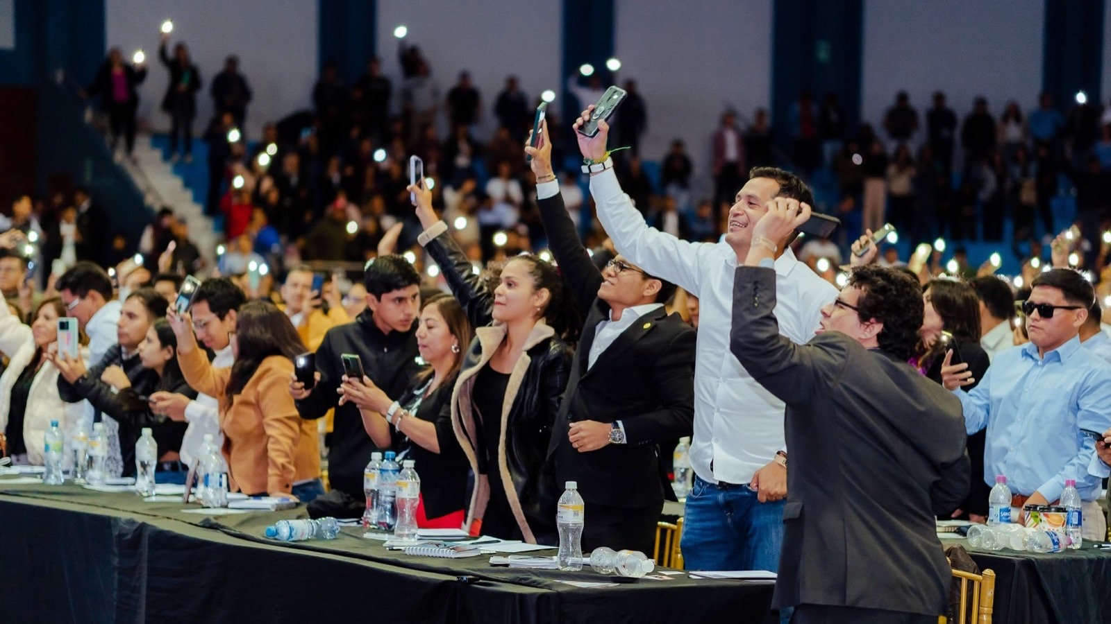 Empresarios de pie con los celulares en alto durante un evento de Negocios Legendarios